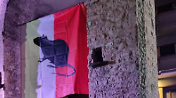 Striscione con un enorme topo al centro issato sull'antica porta della città