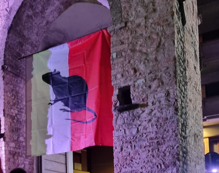 Striscione con un enorme topo al centro issato sull'antica porta della città